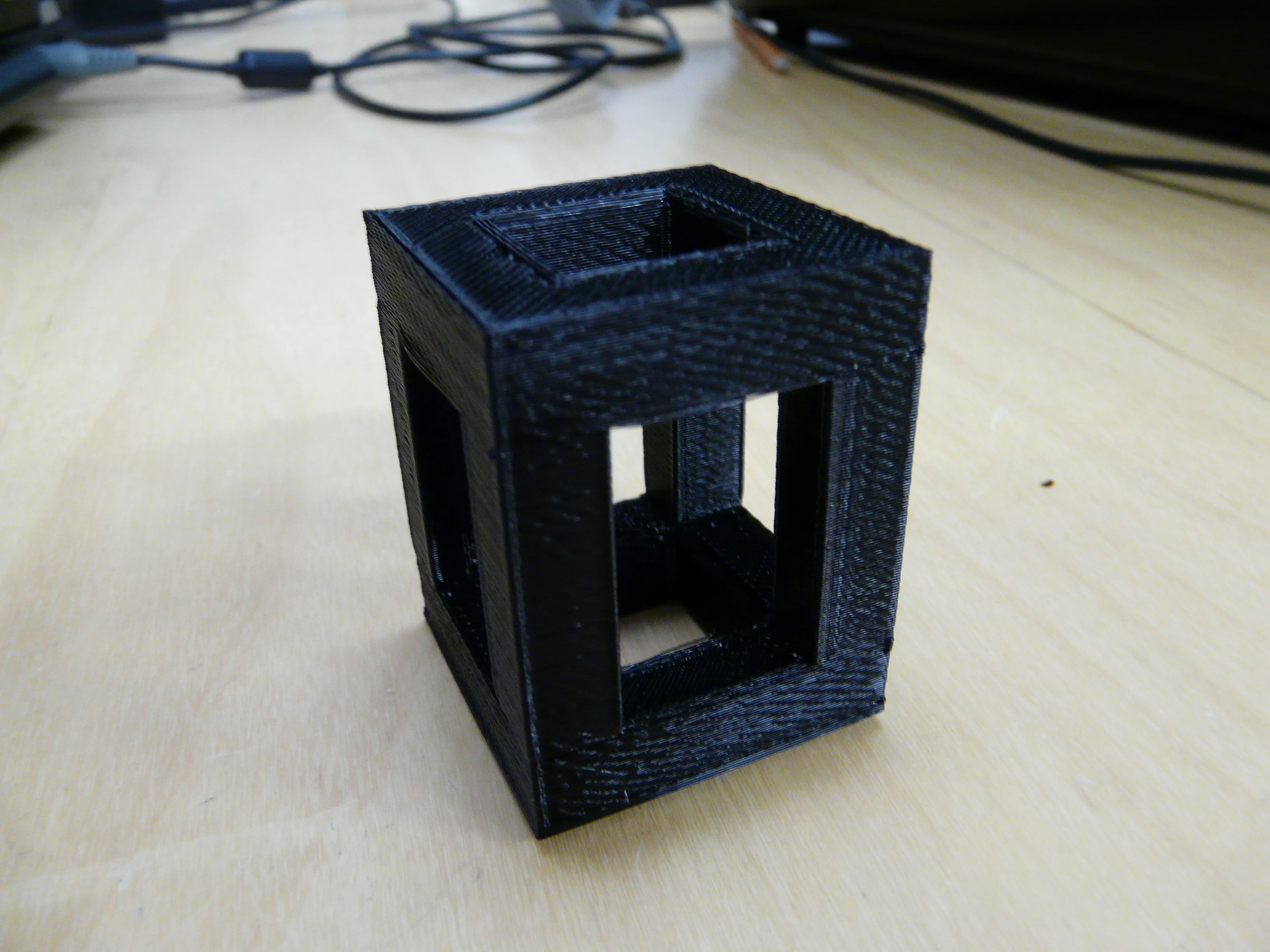 Musta ontto 3D-tulostettu kuutio-osa vaalealla pöydällä.