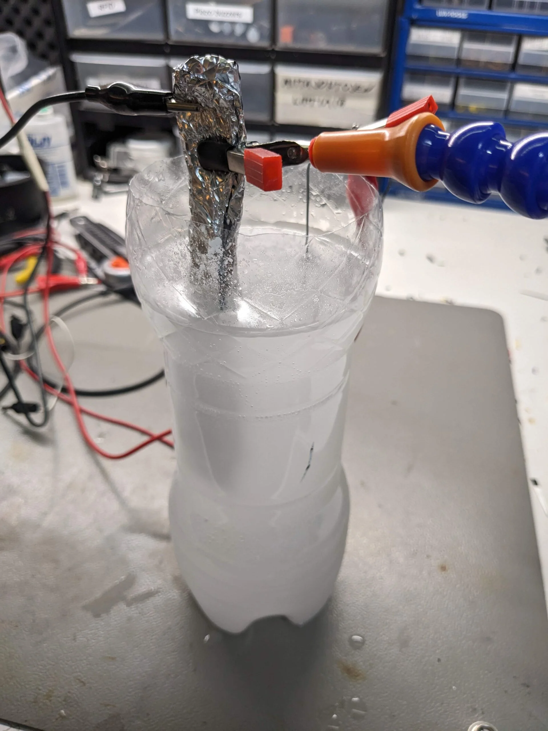 A PET bottle with a milky liquid, where two pieces of metal are submerged, each with a wire clamped to them.